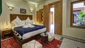 A well-appointed bedroom with a large bed, ornate headboard, and decorative wall sconces. - Deluxe Room #8 (Marrakech)