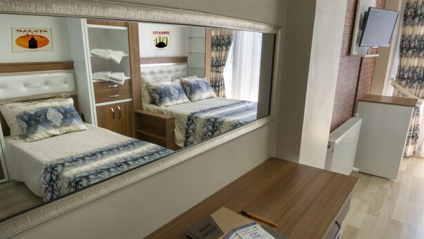A hotel room with a large bed, a wardrobe, a desk with a notebook and pen, and a television. - Koçak Pansiyon (Istanbul)