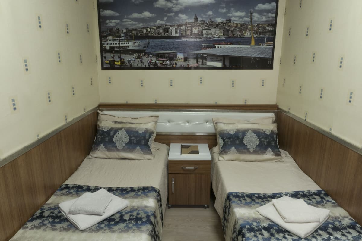 A hotel room with two single beds, a small wooden nightstand, and a large cityscape mural on the wall.