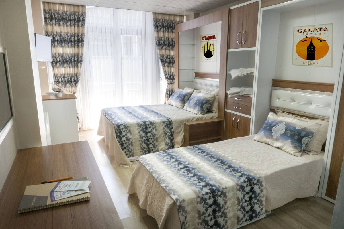 A hotel room with two beds, a desk, a chair, a TV, and a wardrobe.