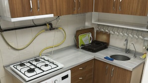A compact kitchen with wooden cabinets, a built-in washing machine, a gas stove, and a sink. - Koçak Pansiyon (Istanbul)