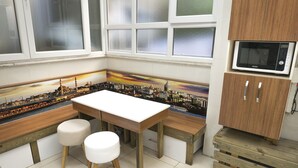 A kitchen with a white table, two stools, a wooden bench, a microwave, and a cabinet. - Koçak Pansiyon (Istanbul)