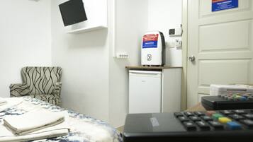 A hotel room with a bed, a chair, a TV mounted on the wall, a mini-fridge, and a control panel.
