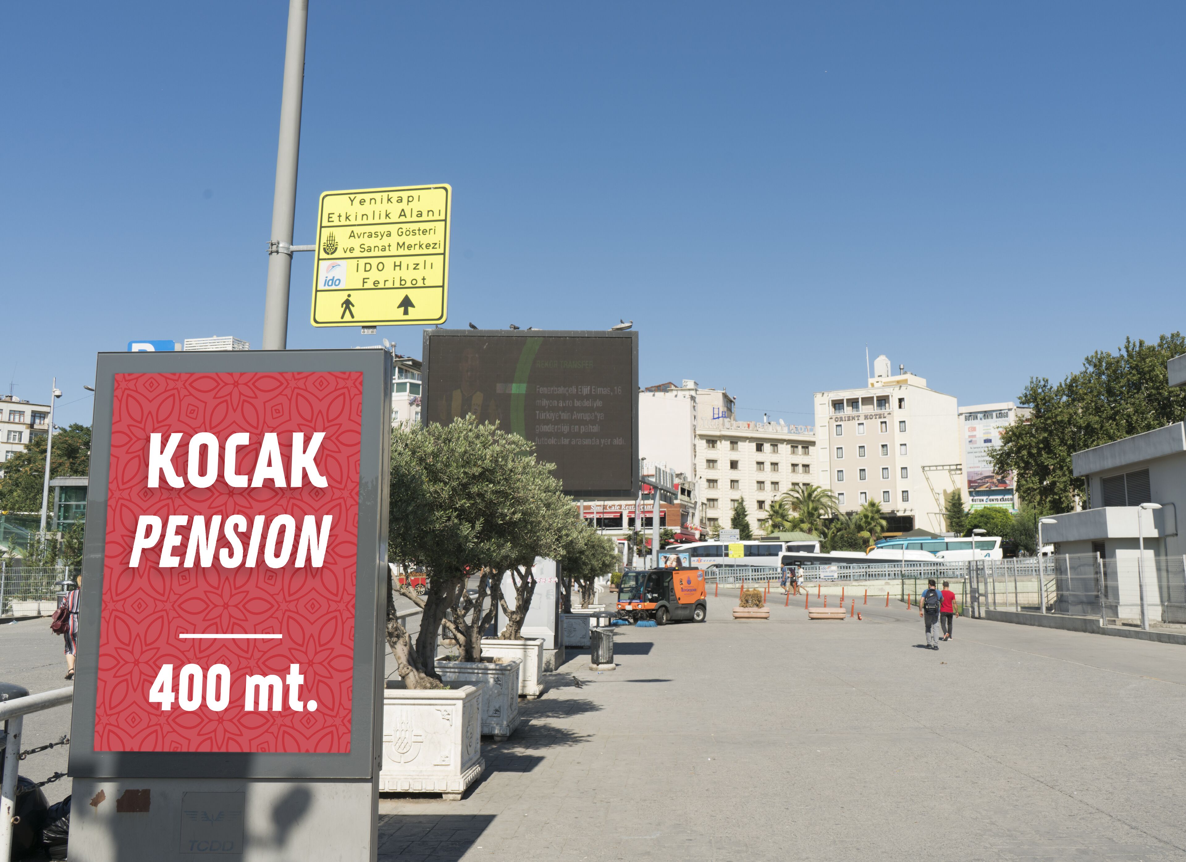 Señal de KOCAK PENSION a 400 metros, con cielo despejado y edificios urbanos al fondo.