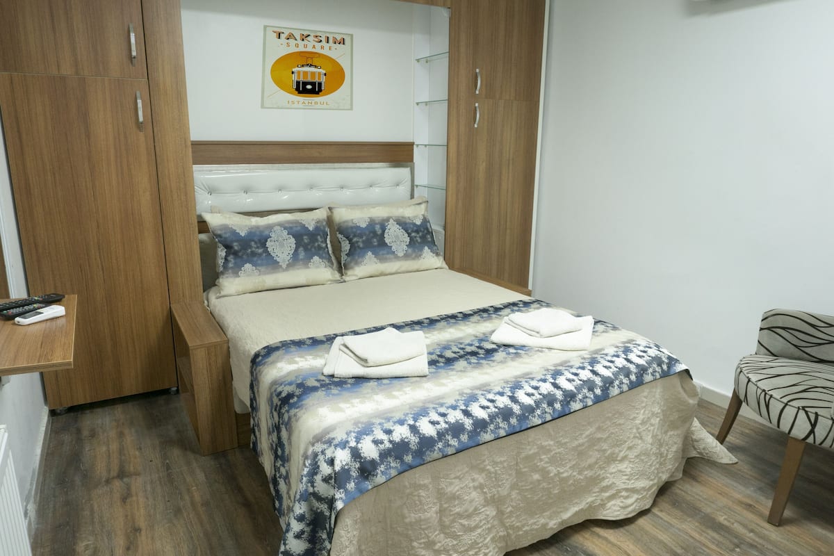 A bedroom with a bed, a wooden wardrobe, a chair, and a wall-mounted sign.