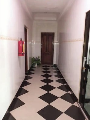 A hallway with a checkered floor, a fire extinguisher on the left, and a door at the end.