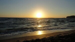 A beach with the sun setting over the ocean, waves gently lapping at the shore. - Beautiful calm rooftop studio with stunning views (CHANIA)