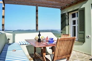 Une terrasse avec une table dressée pour deux personnes, une bouteille de vin et un saladier de fruits.