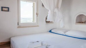 A bedroom with a bed, a window, a white curtain, and a small shelf with a picture frame. - Beautiful calm rooftop studio with stunning views (CHANIA)