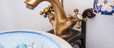 A vintage brass faucet mounted on a wall, a decorative ceramic sink with floral patterns, and a blue and white ceramic container with a floral design.