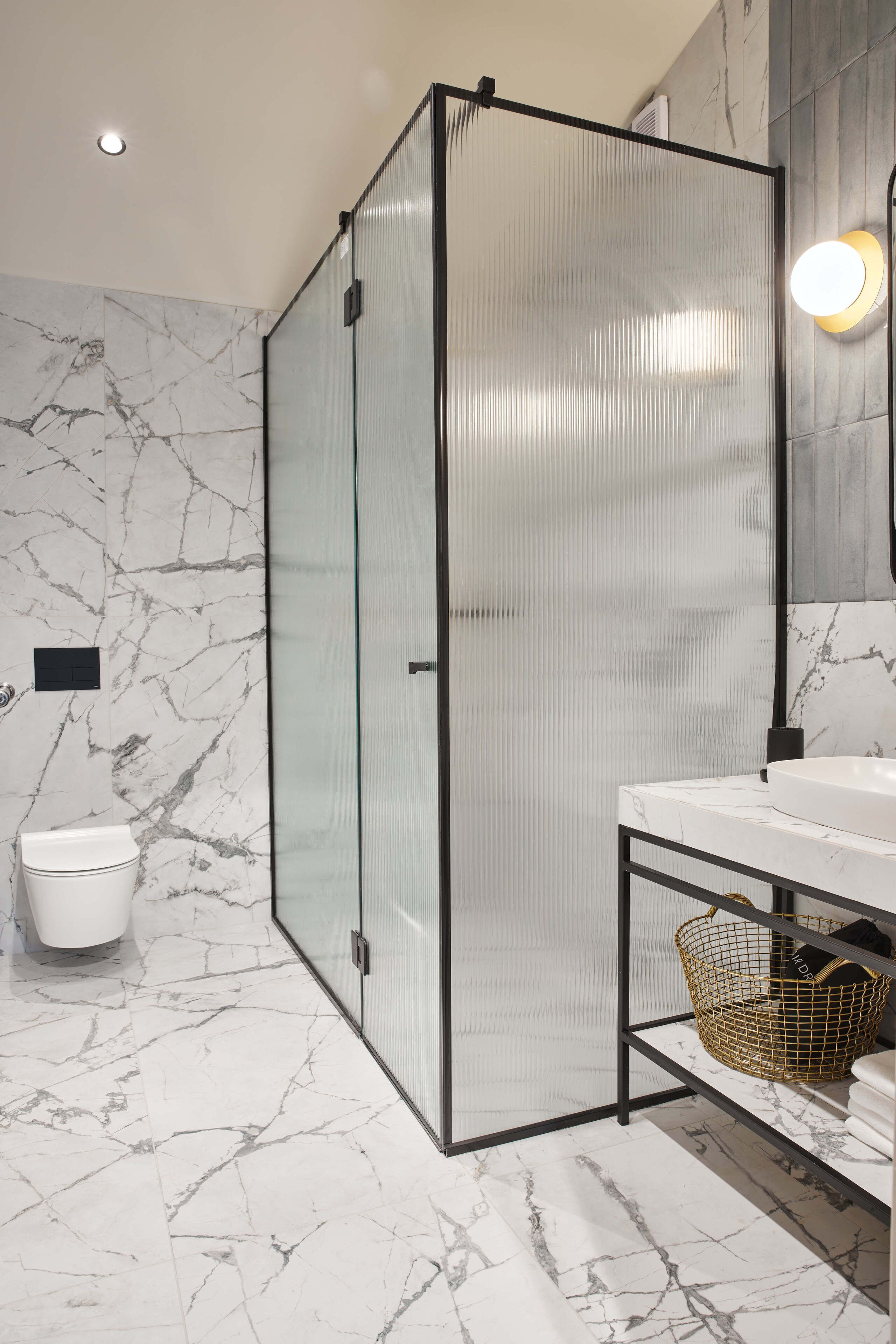 Un baño moderno con cabina de ducha de vidrio, suelo de mármol, inodoro blanco y tocador con encimera de mármol.