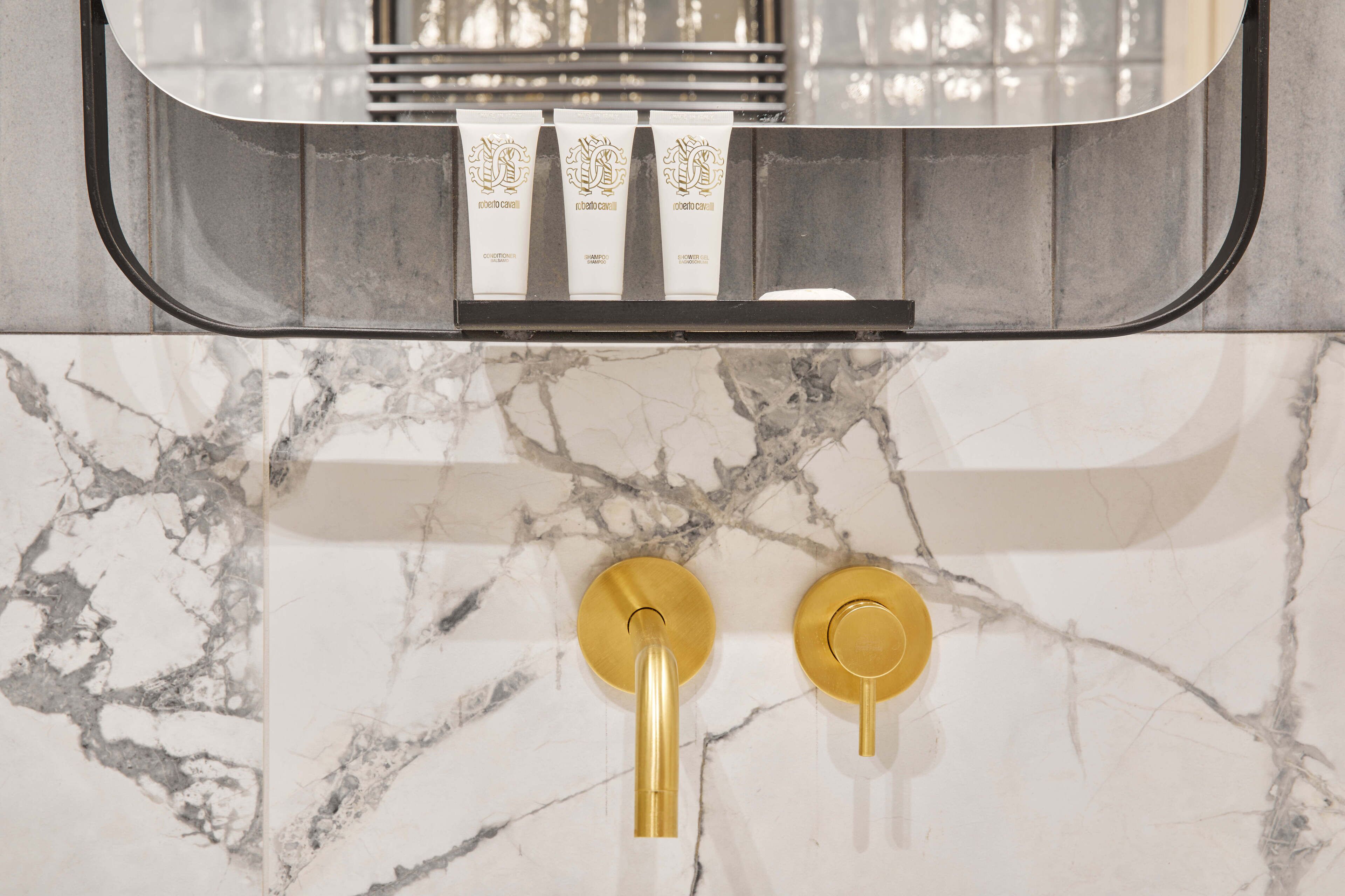A bathroom with marble tiles, a mirror, and two gold faucets.