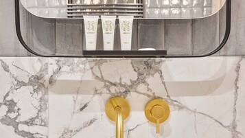 A bathroom with marble tiles, a mirror, and two gold faucets.