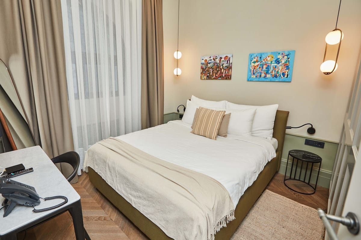 Une chambre d’hôtel comprenant un lit, un bureau avec un téléphone, deux lampes fixées au mur et deux tableaux.