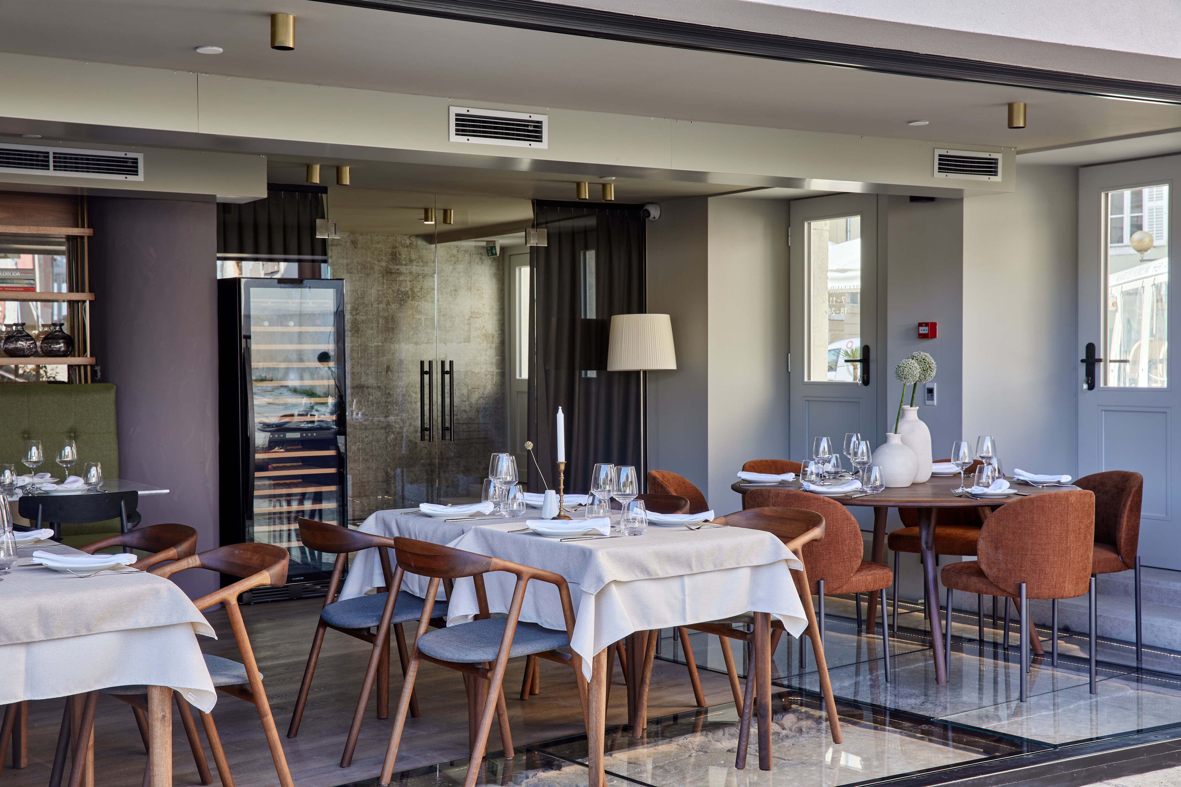 A restaurant with tables set for dining, a bar area, and a large window providing a view.