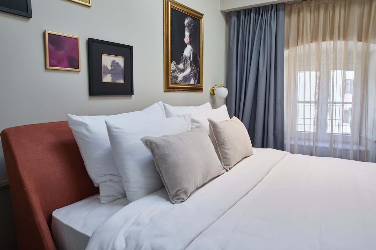 Une chambre d’hôtel avec un lit, des oreillers, un fauteuil rouge et un tableau au mur.