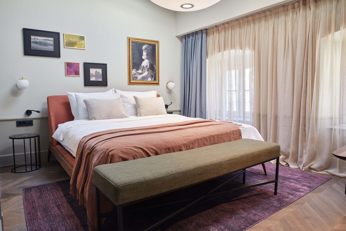 Une chambre à coucher avec un lit, un banc, des tables de chevet et des rideaux.