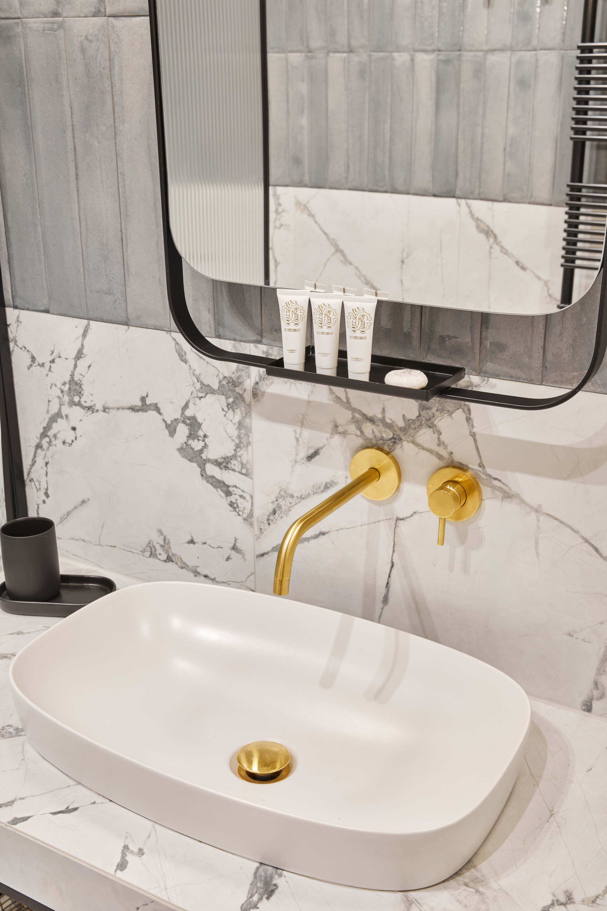 A bathroom with a white sink, gold fixtures, and a marble backsplash.