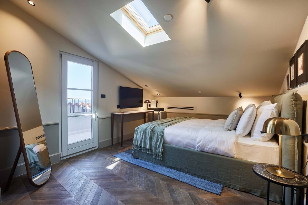 Une chambre à coucher comprenant un lit, un bureau, une chaise, un téléviseur et une fenêtre de toit.