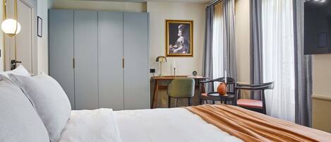 A hotel room with a large bed, a desk, a chair, and a TV on the wall.