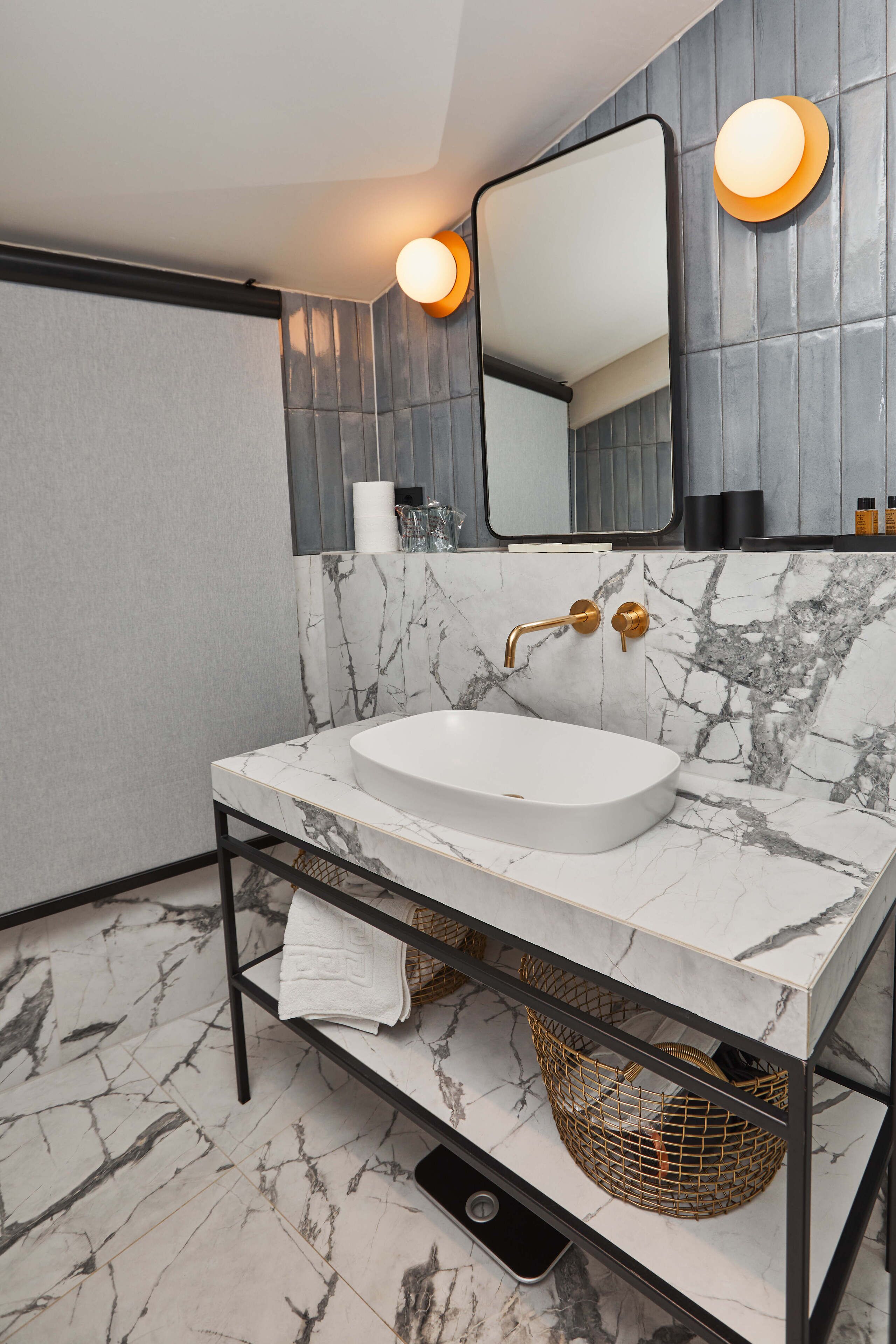 Une salle de bain avec un lavabo en marbre blanc, des robinetteries dorées et un miroir au-dessus.