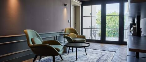A modern lounge area with two armchairs, a small round table, and a large window providing a view of the outdoors.