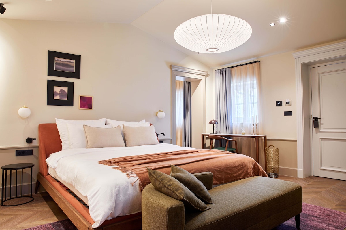 Une chambre d’hôtel avec un lit, un banc, une lampe et une porte.