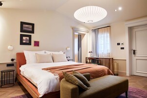 Un dormitorio bien iluminado con una cama grande, una mesita de noche, una lámpara y una silla.