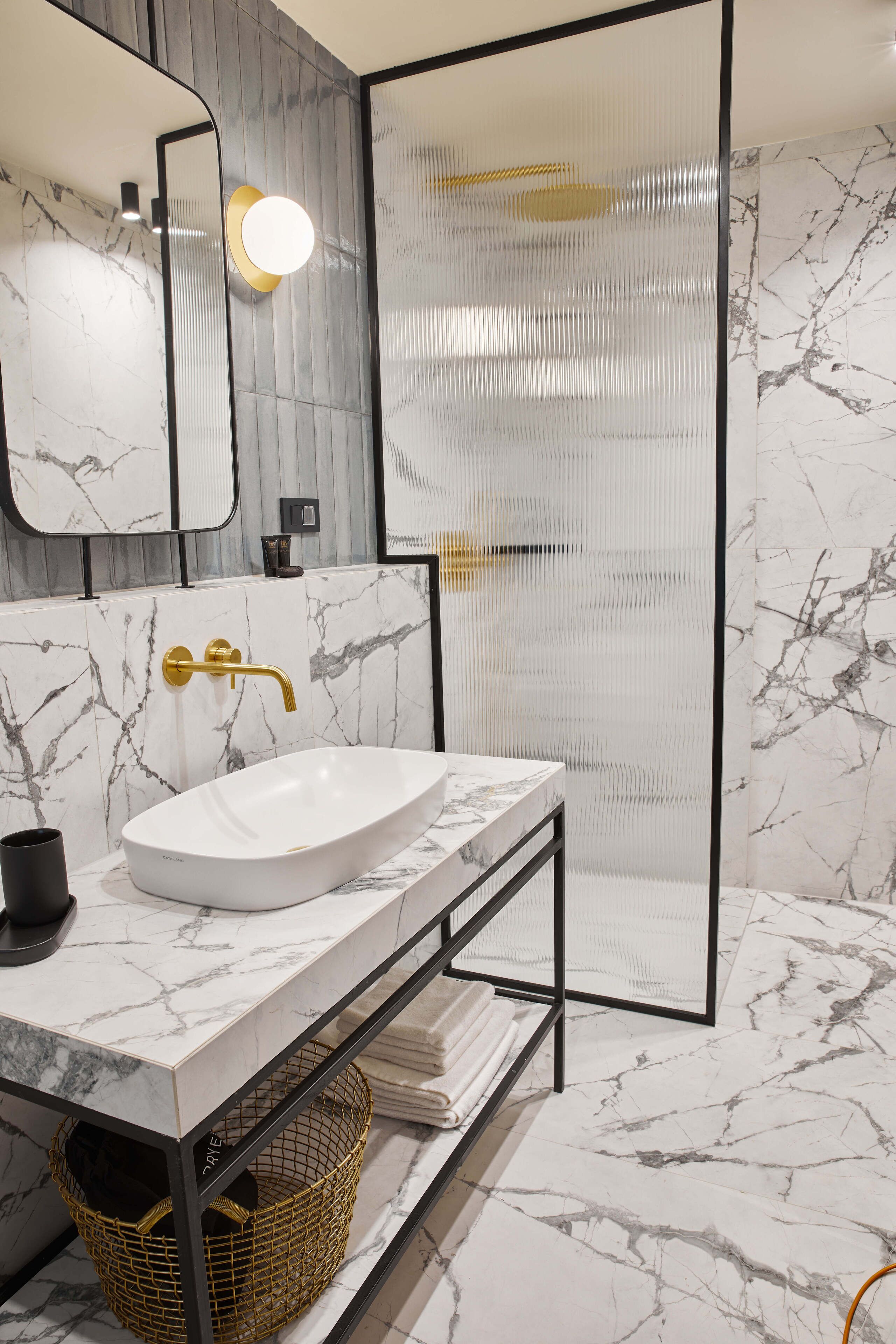 A bathroom with a white marble sink, gold faucet, and a large mirror.