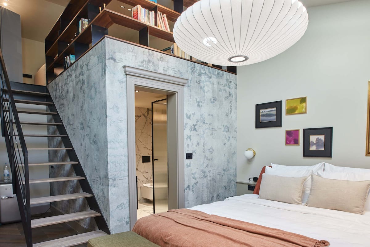 Une chambre à coucher avec un grand lit, un banc, un escalier et une lucarne.