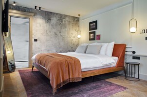 Un dormitorio moderno con una cama grande, piso con estampado de espiga, pared de hormigón y una mesita de noche pequeña.