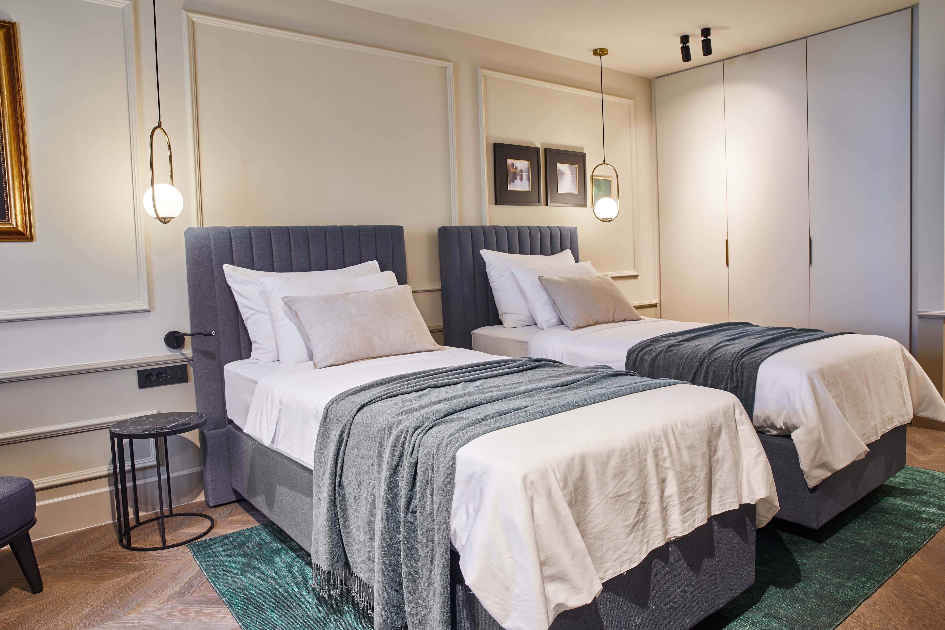 Une chambre moderne avec deux lits, une petite table de chevet, un banc et une armoire.