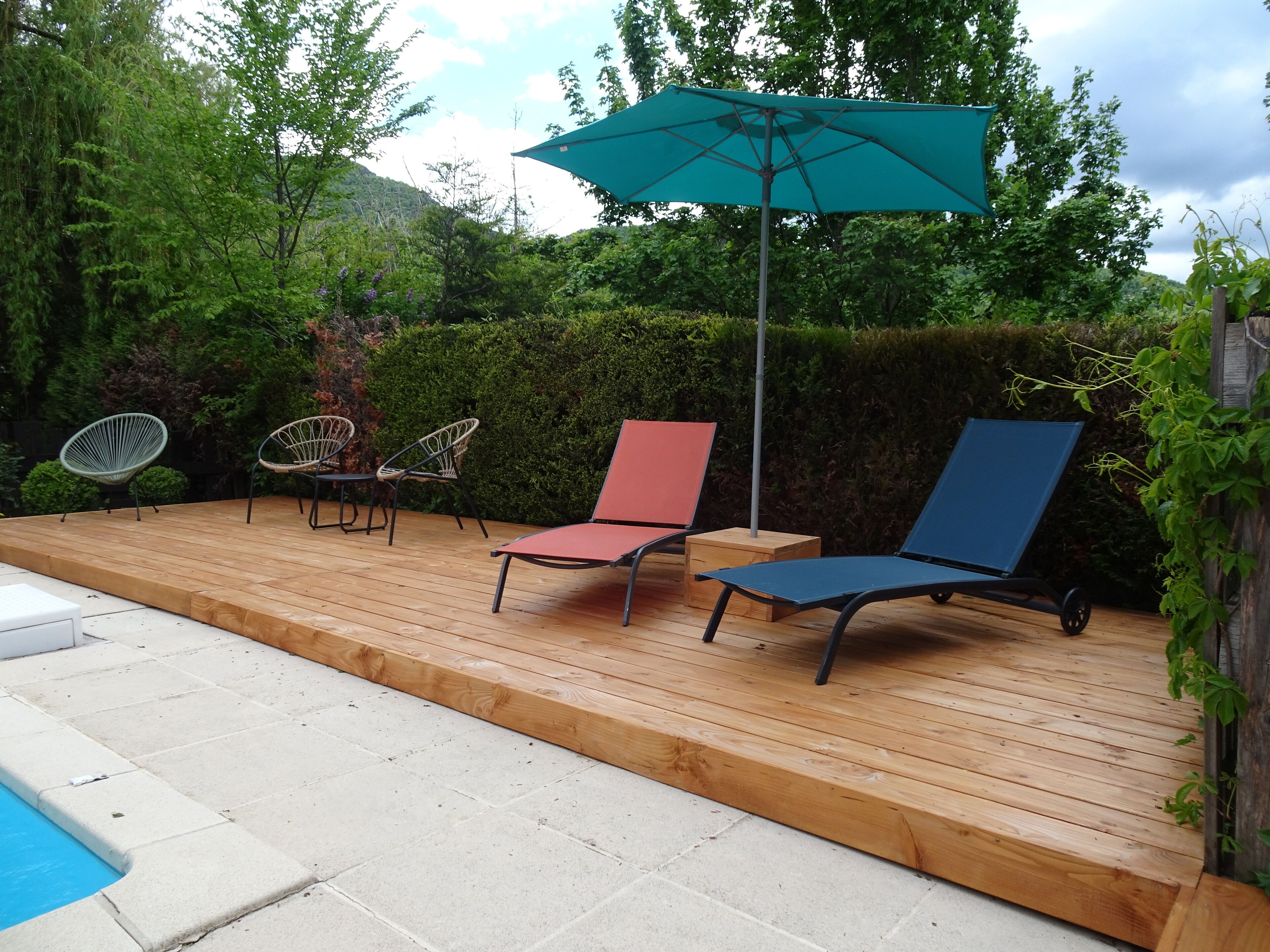 Eine Holzterrasse mit Sitzgelegenheiten im Freien, einem Pool und einem grünen Sonnenschirm.