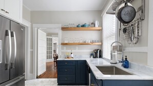 Une cuisine moderne dotée d’un réfrigérateur en acier inoxydable, de meubles de couleur bleu foncé et d’un plan de travail en marbre blanc.