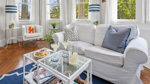 Un salon lumineux, meublé de blanc, avec une table basse en verre et une vue sur la verdure environnante.