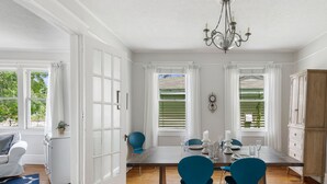 Un coin repas avec une table en bois, deux chaises bleues, des rideaux blancs et un lustre.