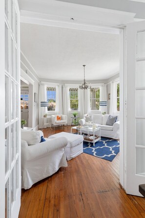 A white-themed living room with a wooden floor, white sofas, a coffee table, and a chandelier. - Urban Chic Living | Resi on Rutledge (Charleston)