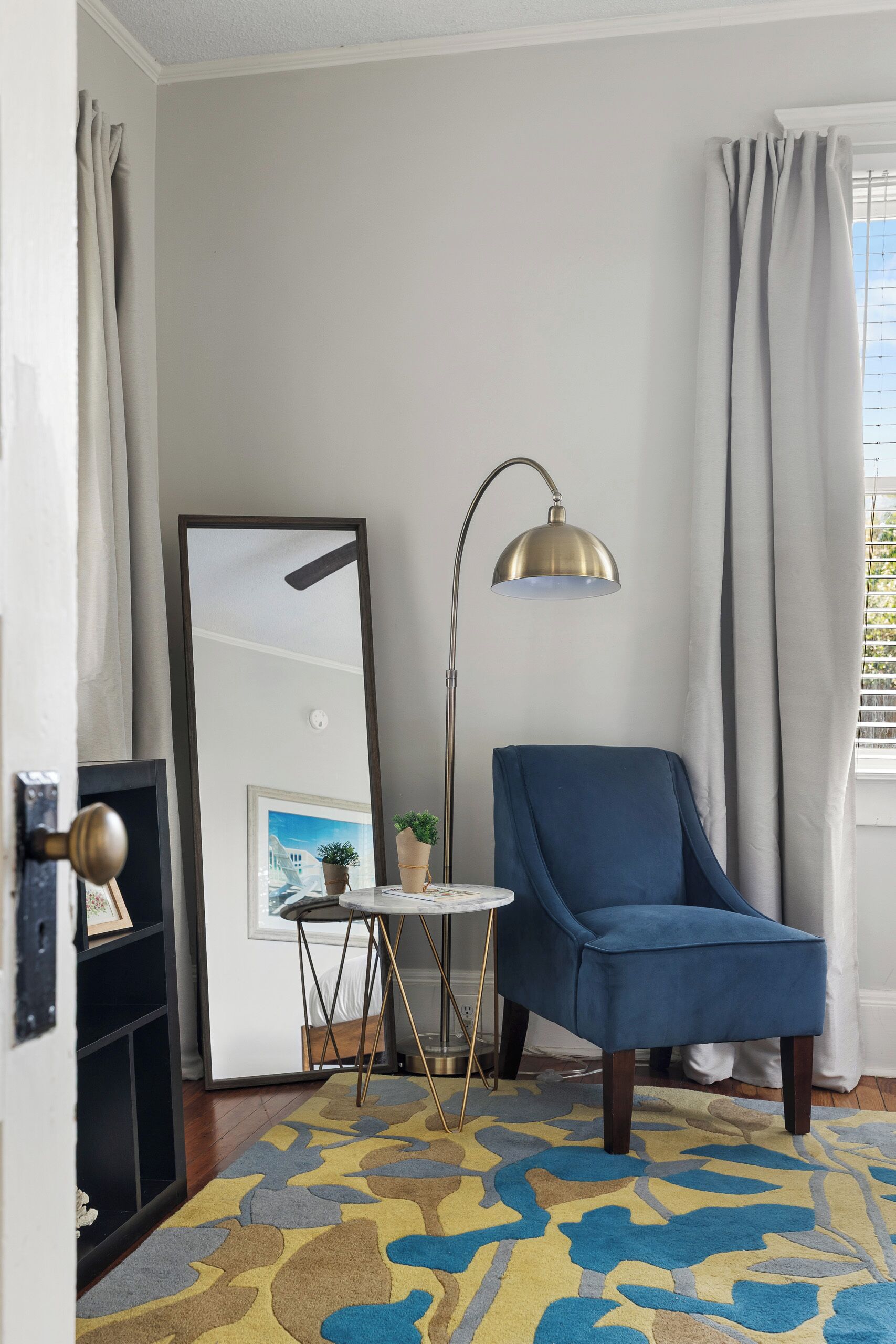 Una habitación con un sillón azul, una lámpara de pie, una mesita con una planta y un cuadro en la pared.