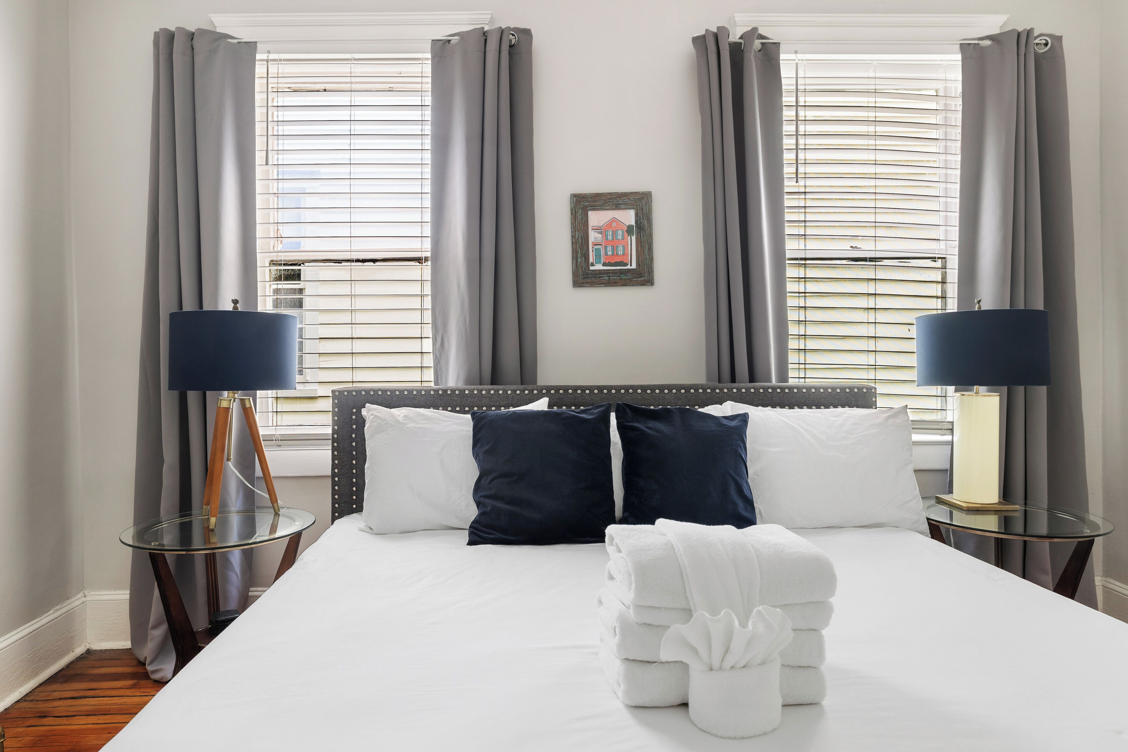 Ein Hotelzimmer mit einem großen Bett, zwei Nachttischlampen, einem gerahmten Bild an der Wand und einem Fenster mit Jalousien.