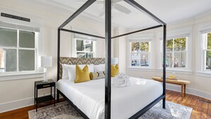 A four-poster bed with a white canopy, a bedside table with a lamp, and a bench with a view of the outside.