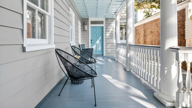 A porch with white railings, a blue door, and two wicker chairs.