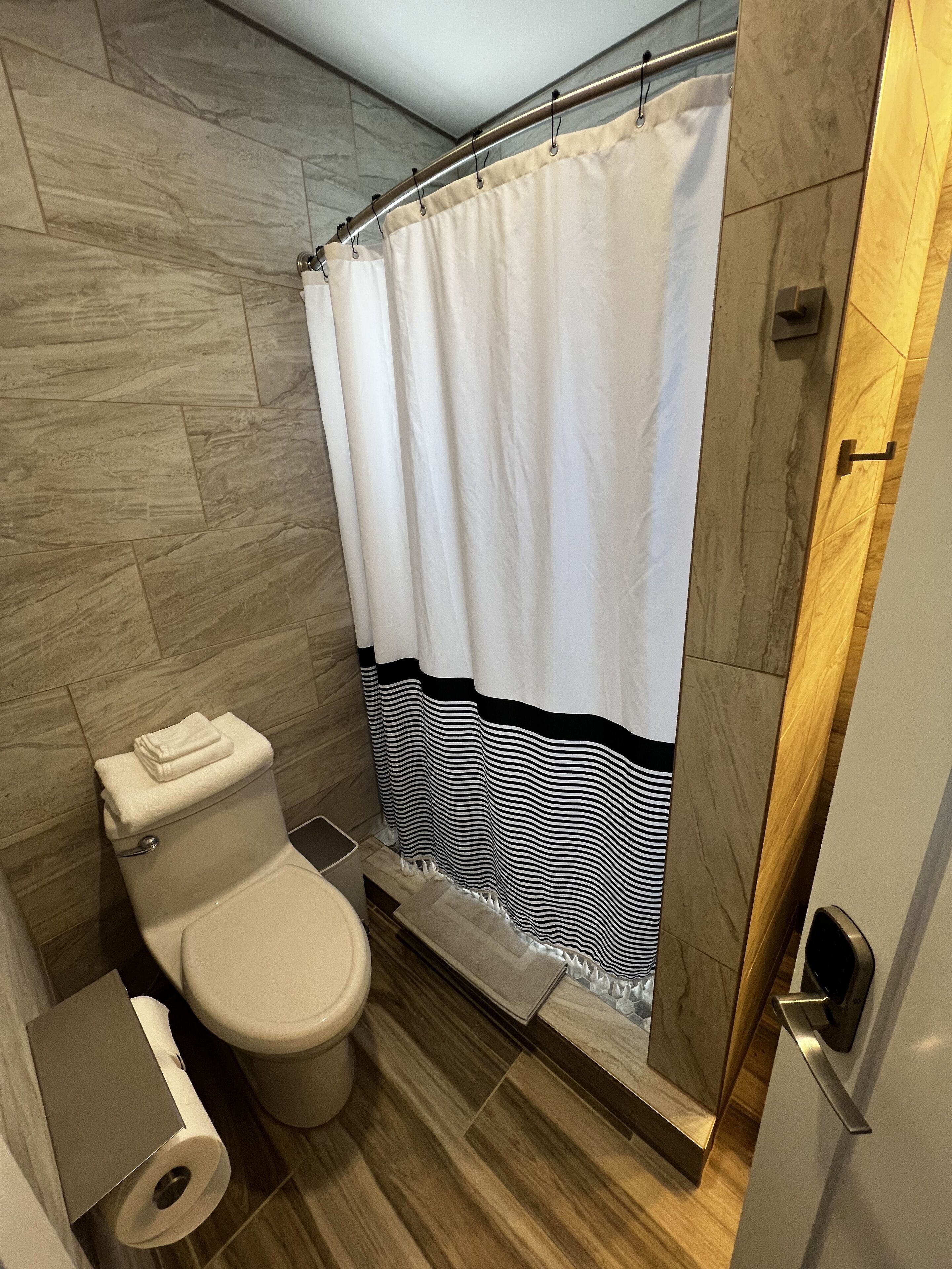 A bathroom with a toilet, a shower curtain, and a wooden floor.
