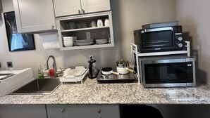 A kitchen with white cabinets, a granite countertop, a sink, and two stacked microwaves.