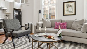 A modern living room with a grey sofa, a black chair, and a round coffee table with a magazine and a bottle. - The Feather | Next To Bad Bunnies Coffee (Charleston)