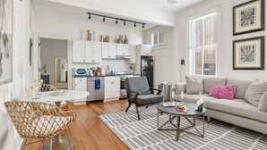 A modern kitchen with white cabinets, a dining table, and a bar area. - The Feather | Next To Bad Bunnies Coffee (Charleston)