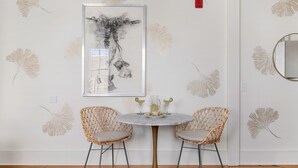 A room with a round table, two wicker chairs, a framed artwork on the wall, and a mirror. - The Feather | Next To Bad Bunnies Coffee (Charleston)