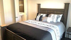 Slaapkamer met houten bedframe, een witte muur, een deur met spiegel en een klein tafeltje naast het bed.