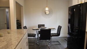 Een moderne keuken met een eettafel, stoelen, een zwarte koelkast en een bijzondere wandversiering.