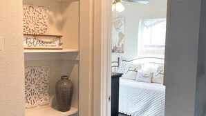 Een gang die leidt naar een slaapkamer met een bed, een kaptafel en een decoratieve wand met een wereldbol en een bord.