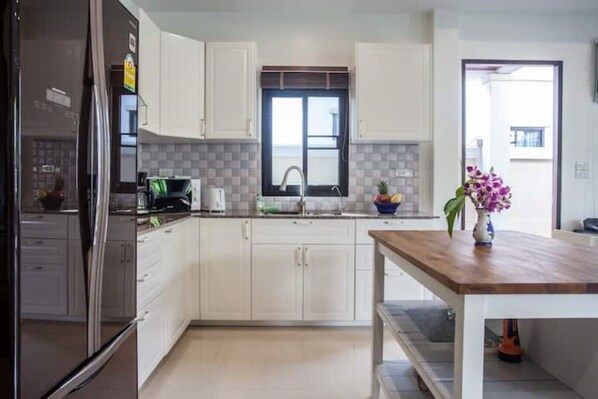 Una cocina moderna con armarios blancos, encimera de madera y ventana sobre el fregadero.